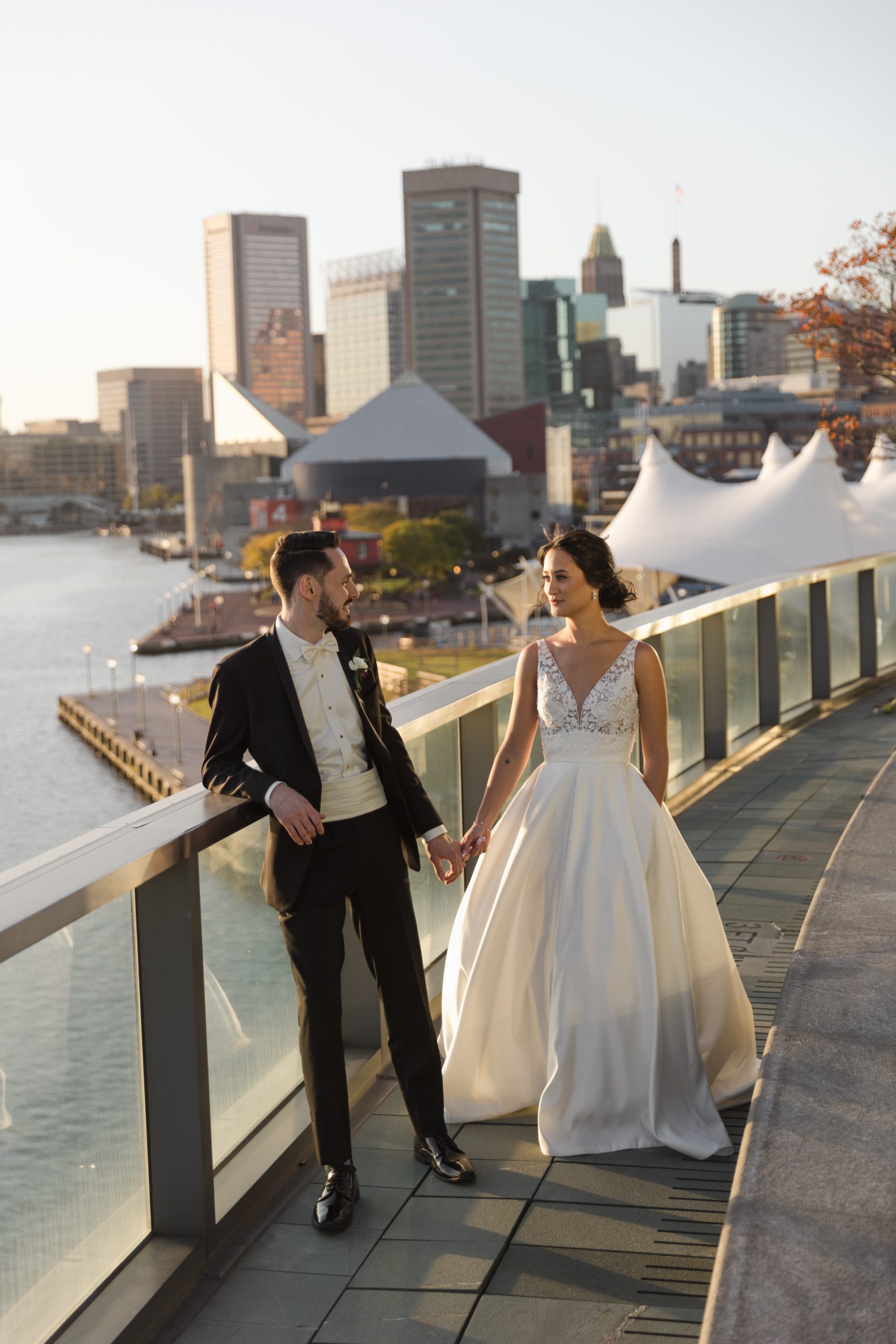 Beautiful couple dressed for their wedding walking outside with Baltimore city in the background.